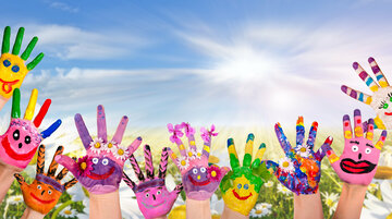 Hände mit gemalten Blumen und Gesichtern in verschiedenen Farben und Stilen recken sich vor einem Hintergrund aus blauem Himmel und weißen Wolken in den Himmel.